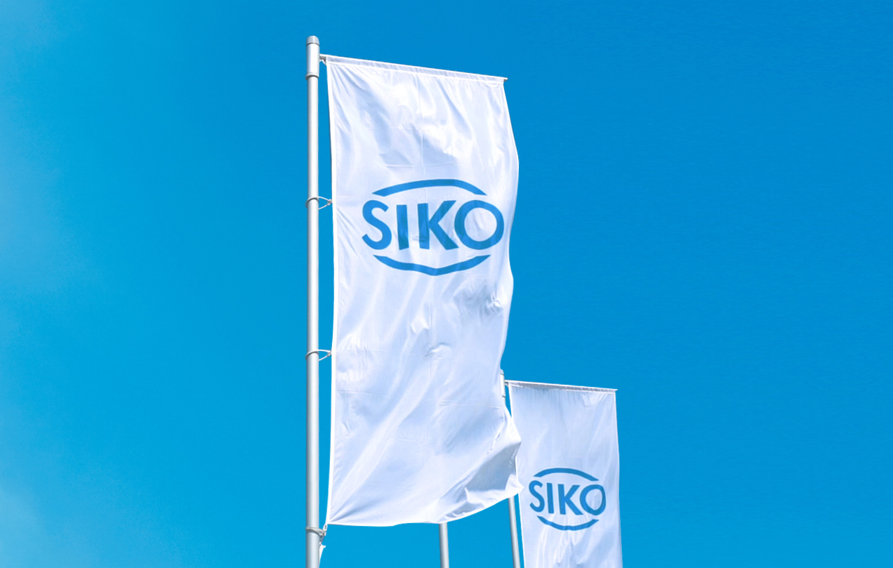 Deux drapeaux blancs avec un logo SIKO bleu flottent au vent